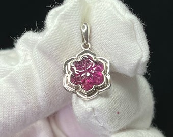 May include: A silver pendant with a pink snowflake-shaped gemstone in the center. The pendant is shaped like a flower with multiple layers of petals.
