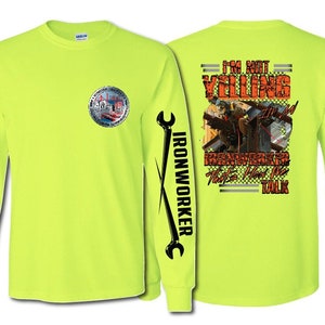 May include: A bright yellow long-sleeve t-shirt with a wrench graphic on the left sleeve and the text "IRONWORKER" on the right sleeve. The back of the shirt features a graphic of an ironworker on a bridge with the text "I'M NOT YELLING IT'S HOW WE TALK".