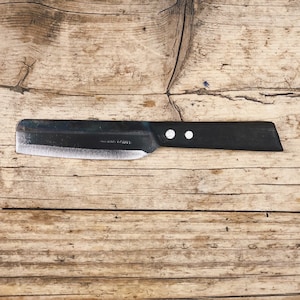 Può includere: Un coltello con manico nero e lama argentata su una superficie di legno.