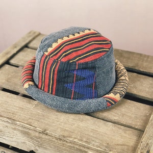 Puede incluir: Un sombrero de cubo gris y negro con un patrón tejido colorido. El sombrero tiene un ala ancha y una corona plana.