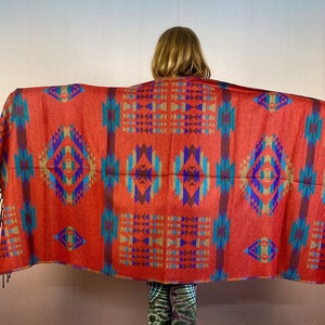 May include: A red, blue, and gold patterned shawl with fringe. The shawl has a geometric design with a diamond pattern.