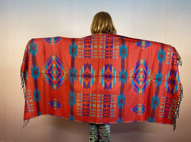 May include: A red, blue, and gold patterned shawl with fringe. The shawl has a geometric design with a diamond pattern.