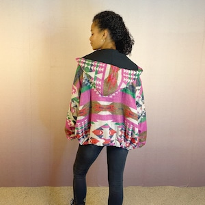 Peut inclure: Une veste à capuche à motif rose, vert et marron avec une doublure noire. La veste a un cordon de serrage à la taille.