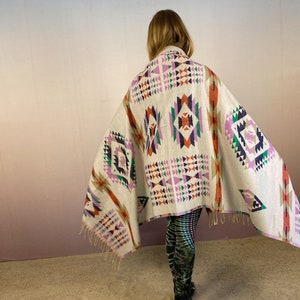 May include: A white throw blanket with a geometric pattern in shades of pink, orange, green, and blue. The blanket has fringe on the edges.