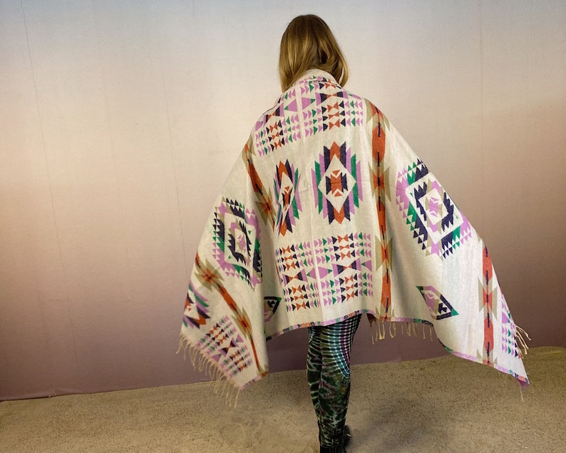 May include: A white throw blanket with a geometric pattern in shades of pink, orange, green, and blue. The blanket has fringe on the edges.