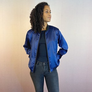 May include: A blue satin bomber jacket with a zip closure. The jacket has a black ribbed collar and cuffs.