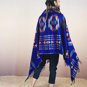 May include: A blue and red patterned shawl with fringe. The shawl is draped over a person's shoulders and is worn with black pants.