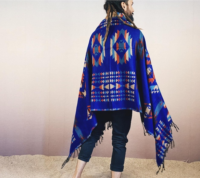 May include: A blue and red patterned shawl with fringe. The shawl is draped over a person's shoulders and is worn with black pants.