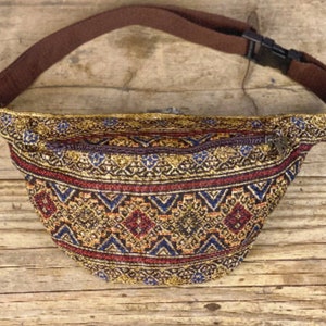 Könnte beinhalten: Eine braune Bauchtasche mit Reißverschluss und einem gemusterten Stoff in Gold, Rot und Blau.