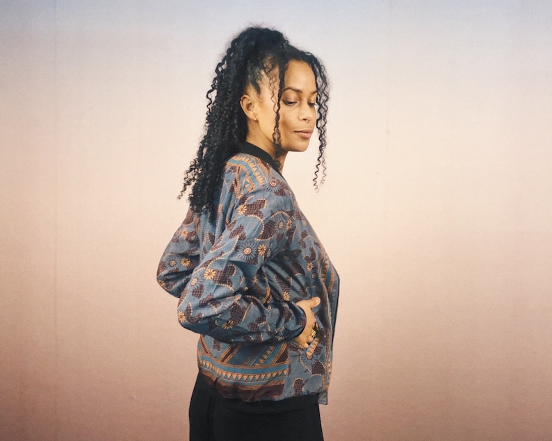 May include: A blue and brown patterned bomber jacket with a black collar and cuffs. The jacket features a floral and geometric design. The jacket is worn by a person.