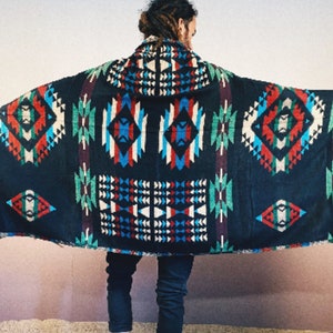May include: A black hooded blanket with a colorful geometric pattern. The pattern features red, blue, green, and white colors. The blanket has fringe on the edges.