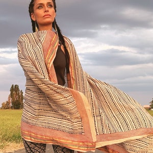 May include: A woman wearing a white and black striped shawl with red and yellow accents. The shawl is draped over her shoulders and flowing in the wind.