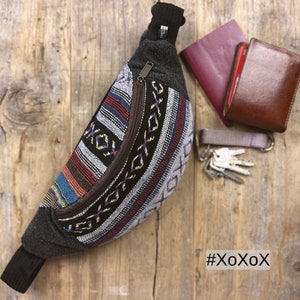 May include: A black and grey fanny pack with a zipper closure and a colourful woven pattern. The fanny pack is on a wooden surface with a passport and keys.