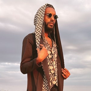 May include: A person wearing a black hooded jacket with a white and black patterned scarf, round sunglasses, and a floral patterned shirt.