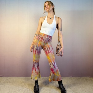 May include: A woman wearing a white halter top and tie-dye bell bottom pants. She is wearing a silver chain belt and a brown leather shoulder bag.