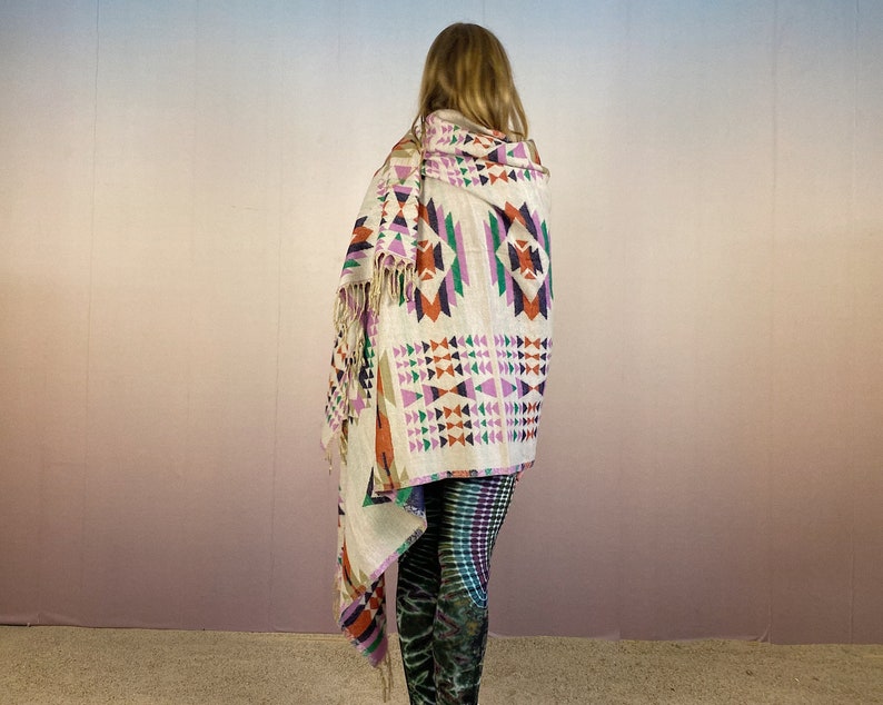 May include: A white throw blanket with a geometric pattern in shades of orange, purple, green, and blue. The blanket has fringe on the edges.