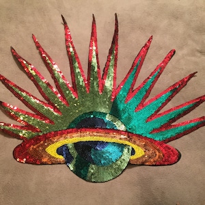 May include: A colorful sequined patch featuring a stylized globe with a ring around it, surrounded by red and green rays.