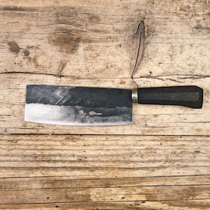 May include: A black-handled butcher knife with a silver blade sits on a wooden surface.