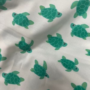 May include: White fabric with a repeating pattern of green sea turtles. The turtles have yellow accents and are facing different directions.