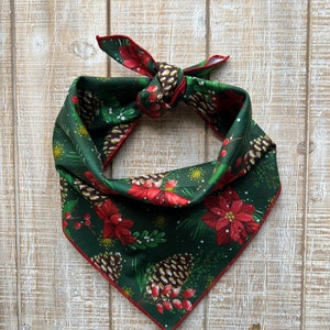 May include: A green bandana with a red trim and a Christmas-themed print of pine cones, poinsettias, and holly berries.