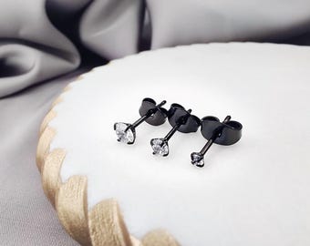 May include: Three stud earrings featuring round, clear, faceted stones set in black metal posts. Each earring includes a matching black metal butterfly-style back closure. The stones are arranged in a row, showing varying sizes from largest to smallest.