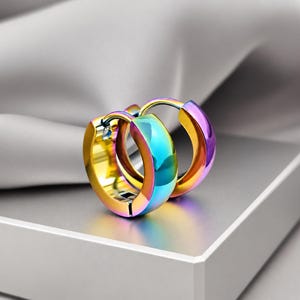 May include: A pair of small hoop earrings featuring a polished, iridescent finish that transitions through shades of gold, blue, and purple. The earrings have a thick, rounded band design with a hinged closure mechanism visible on the side.