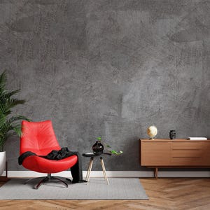 May include: A red swivel chair with a black throw blanket sits in front of a gray textured wall. A wooden cabinet with three drawers is on the right side of the image. A potted plant is on the left side of the image.