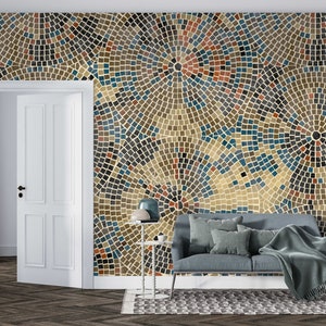 May include: A living room interior design featuring a wall covered in a mosaic pattern wallpaper with blue, brown, and beige tiles. A gray couch with pillows and a throw blanket is placed in front of the wall. A side table with a lamp and a floor lamp are also visible.