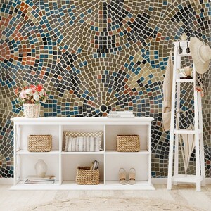 May include: A white bookshelf with three shelves, filled with baskets, books, and shoes. The bookshelf is in front of a wall with a mosaic pattern of brown, blue, and red tiles.