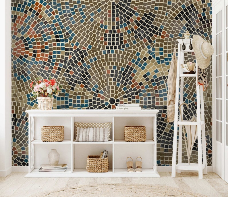 May include: A white bookshelf with three shelves, filled with baskets, books, and shoes. The bookshelf is in front of a wall with a mosaic pattern of brown, blue, and red tiles.