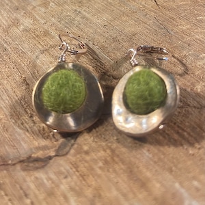 May include: A pair of earrings with a green felt ball in a gold metal setting. The earrings have a hook closure.