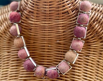 Könnte beinhalten: Eine Halskette aus rosa und beigefarbenen Filzkugeln, die in silberne quadratische Rahmen gefasst sind.