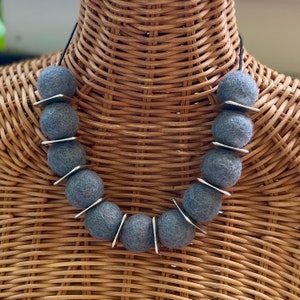 Peut inclure: Un collier de perles en feutre gris avec des accents en métal argenté. Le collier est sur un mannequin.