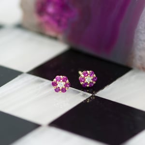 Może przedstawiać: Para złotych kolczyków w kształcie kwiatu z różowymi kamieniami szlachetnymi i pojedynczym białym diamentem w środku każdego kwiatu.