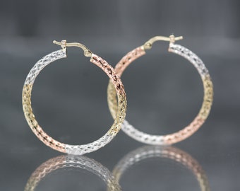 Op de afbeelding: Een paar gouden creolen met een textuurontwerp. De oorbellen zijn gemaakt van drie verschillende kleuren goud: geel, wit en rosé.