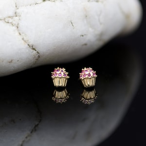 May include: A pair of gold cupcake earrings with pink cubic zirconia stones. The earrings are small and delicate, and they would make a great gift for a friend or loved one.