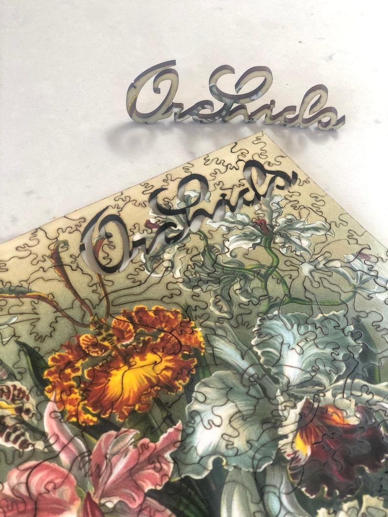 May include: A close-up of a jigsaw puzzle featuring a vintage illustration of orchids. The puzzle pieces are cut in a unique, intricate pattern. The word "Orchids" is spelled out in wooden letters above the puzzle.