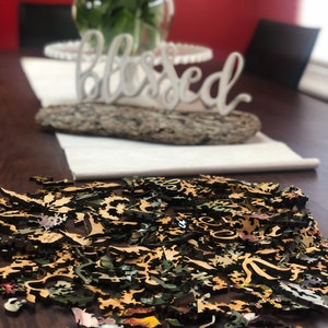 May include: A wooden jigsaw puzzle with a floral design, scattered on a dark wooden table. The puzzle pieces are in various shades of brown, green, and yellow. The word "blessed" is visible in the background.