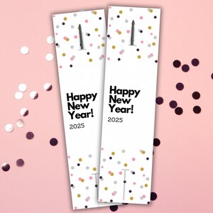 May include: Two white cardstock bookmarks with a confetti pattern in pink, gold, and black. The bookmarks have the text "Happy New Year! 2025" printed on them.