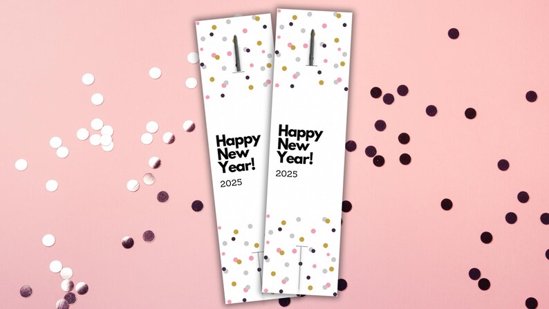 May include: Two white cardstock bookmarks with a confetti pattern in pink, gold, and black. The bookmarks have the text "Happy New Year! 2025" printed on them.