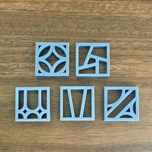 Op de afbeelding: Vijf grijze geometrische tegelonderzetters met verschillende patronen. De onderzetters zijn gemaakt van een glad, stevig materiaal.