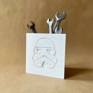 May include: White plastic desk organiser shaped like a Star Wars Stormtrooper helmet with four spanners sticking out of the top.