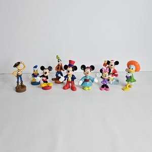 Op de afbeelding: Een verzameling van negen kleine plastic figuurtjes van populaire Disney-personages, waaronder Mickey Mouse, Minnie Mouse, Donald Duck, Goofy en Woody uit Toy Story. De figuurtjes staan allemaal in verschillende poses en zijn felgekleurd.