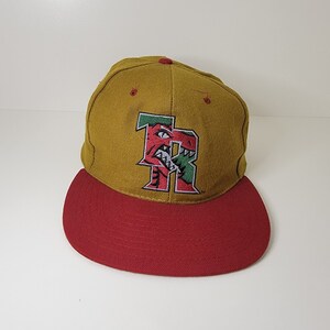 Peut inclure: Une casquette de baseball dorée et rouge avec un logo brodé vert et rouge représentant une tête de dinosaure avec la lettre "R" à l'intérieur de la bouche.