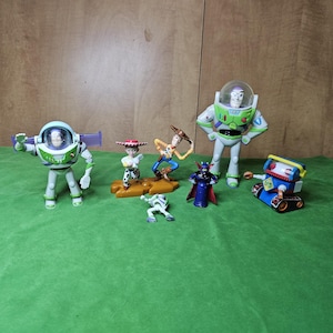 May include: A collection of seven Toy Story character figurines, including Buzz Lightyear, Woody, Jessie, and Zurg. The figurines are made of plastic and are painted in bright colours. They are all standing on a green surface.