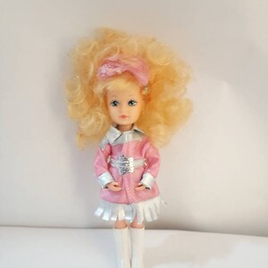 May include: A vintage doll with blonde curly hair, wearing a pink dress with silver trim and white boots.
