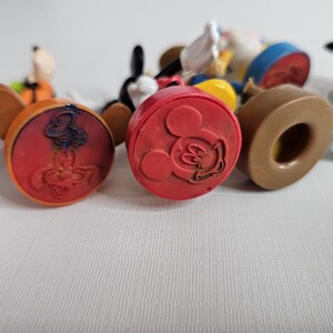 Op de afbeelding: Een verzameling kleurrijke plastic Disney-figuren met een rode, oranje en bruine basis. De figuren zijn Mickey Mouse, Donald Duck, Goofy en Pluto.