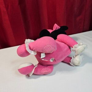 K&ouml;nnte beinhalten: Rosa Pl&uuml;schtier mit schwarzen Ohren und einer wei&szlig;en Schleife. Das Spielzeug liegt auf dem R&uuml;cken mit den Beinen in der Luft. Das Spielzeug hat einen wei&szlig;en Fleck auf der Brust und einen wei&szlig;en Fleck an jedem Fu&szlig;.