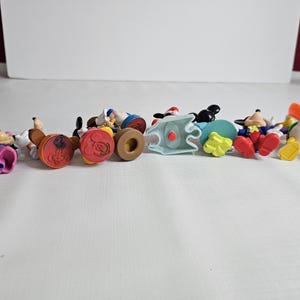 Op de afbeelding: Een verzameling van negen kleine plastic Disney-figuren. De figuren omvatten Mickey Mouse, Minnie Mouse, Donald Duck, Goofy en Pluto. De figuren staan allemaal in verschillende poses en zijn felgekleurd.