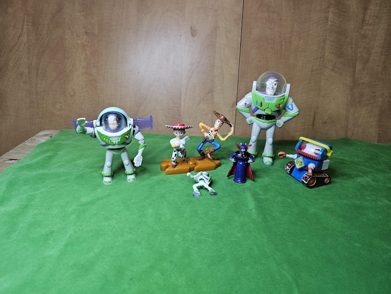 May include: A collection of seven Toy Story character figurines, including Buzz Lightyear, Woody, Jessie, and Zurg. The figurines are made of plastic and are painted in bright colours. They are all standing on a green surface.